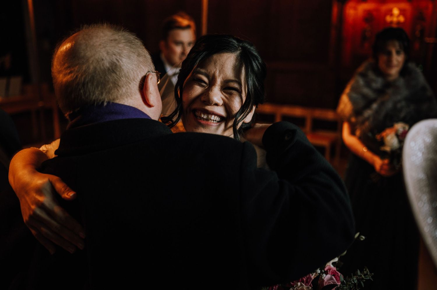 Joyful moment captured during wedding reception with warm red ambient lighting.