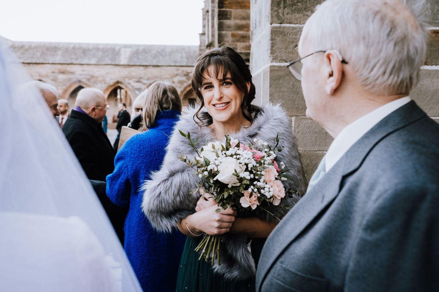 A guest holding a floral bouquet chats with others during a wedding reception.