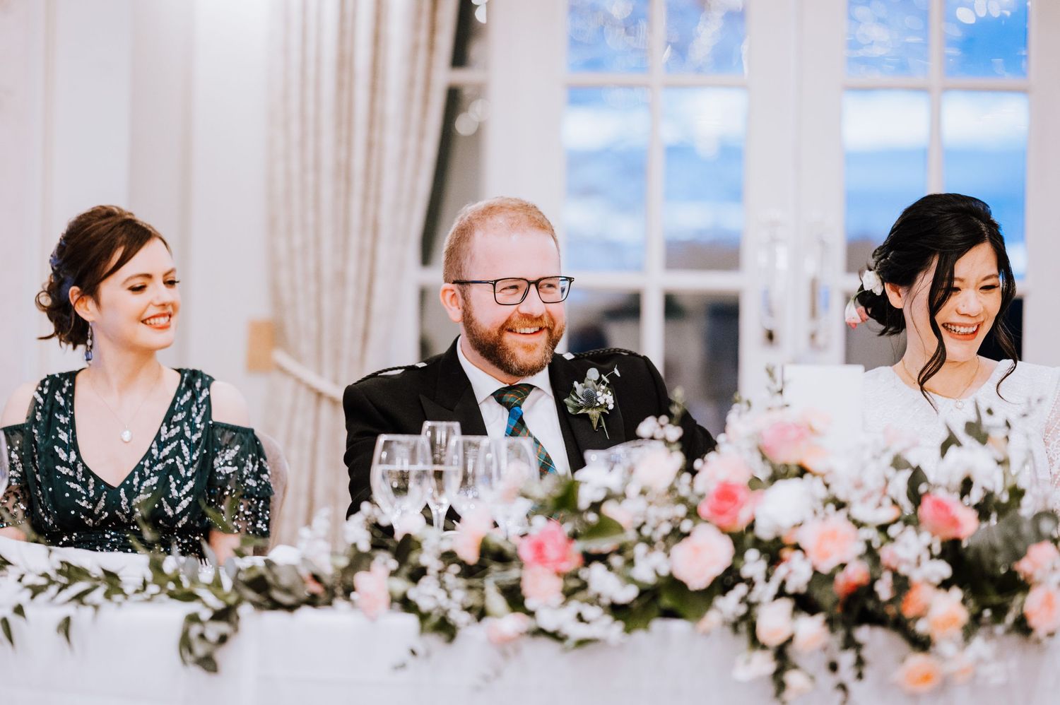 Wedding party seated at head table with pink floral centerpieces and elegant decor.