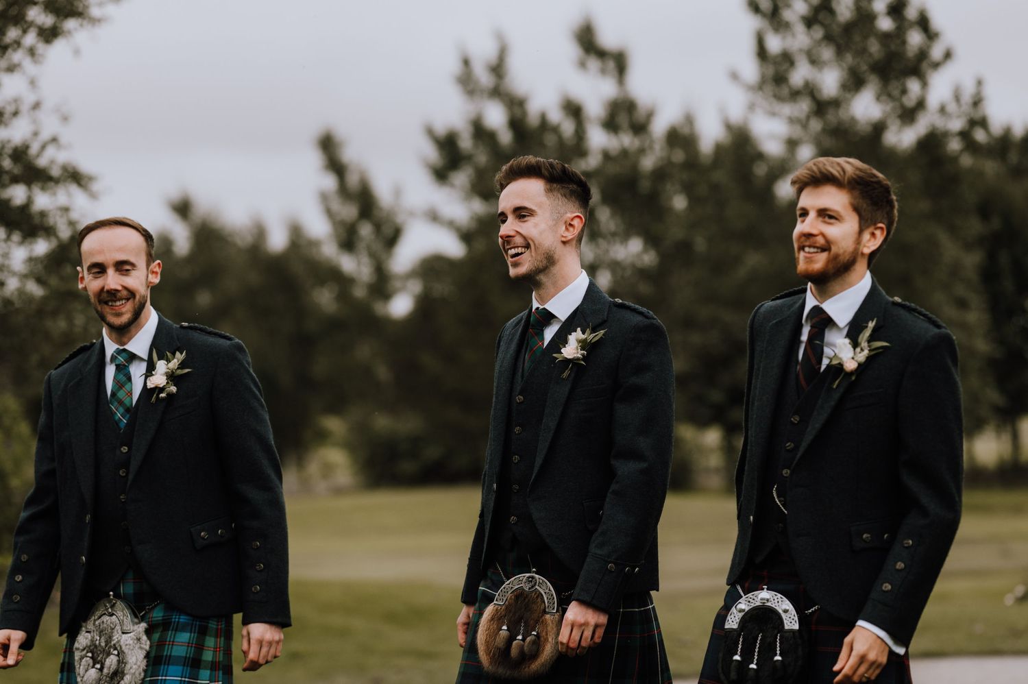 Groomsmen in traditional Scottish formal wear with kilts outdoors.