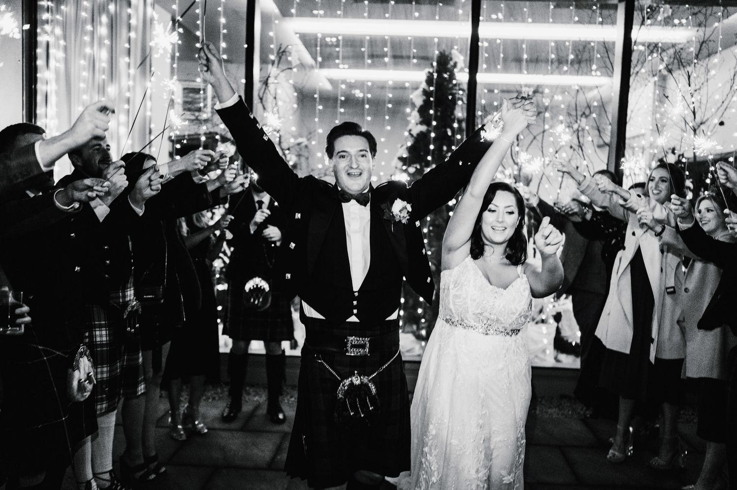 Newlyweds celebrate with raised arms during their wedding exit as guests shower them with sparklers and confetti.