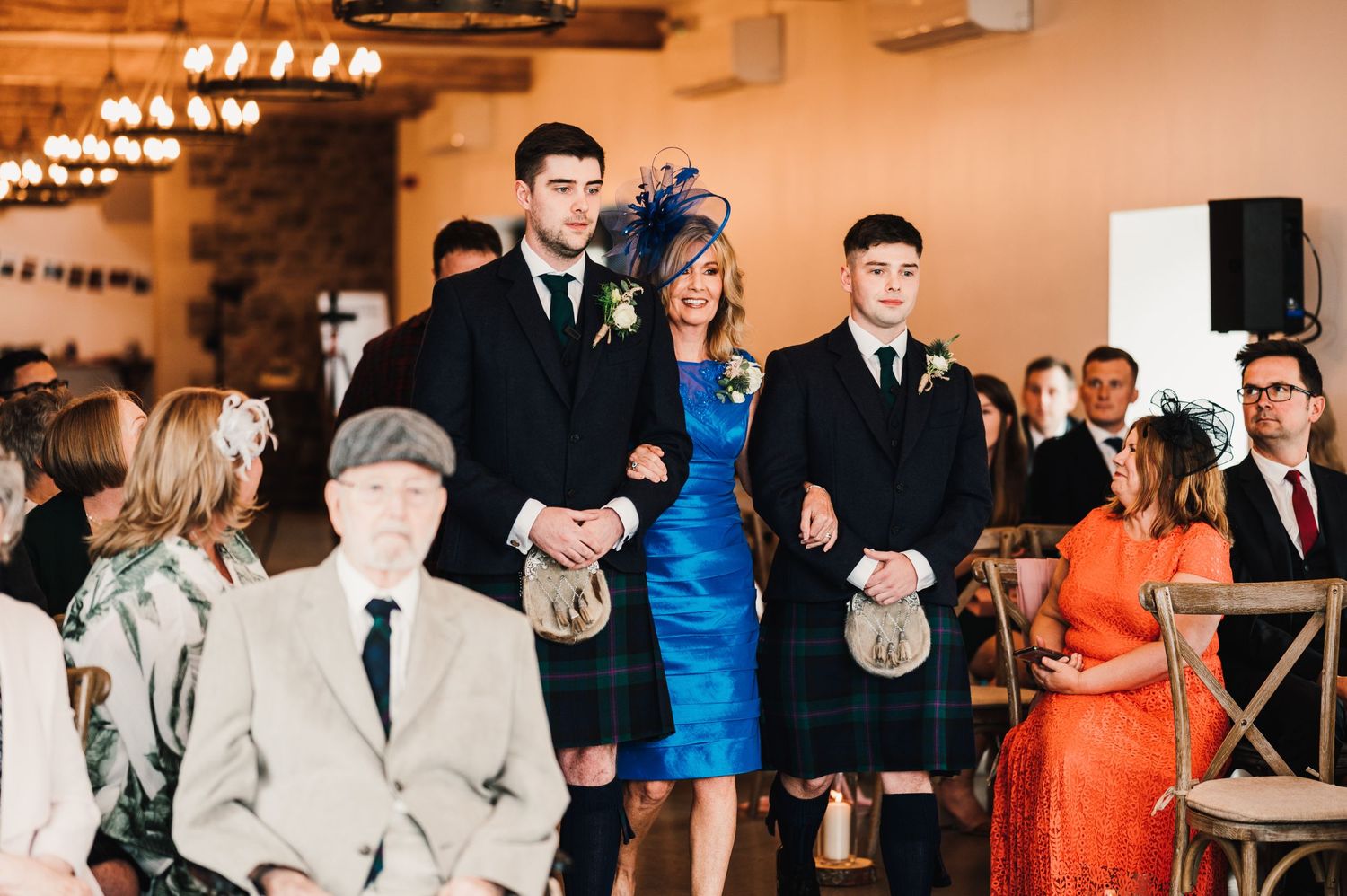Wedding guests watching as someone in a blue dress and formal attire walks down the aisle.