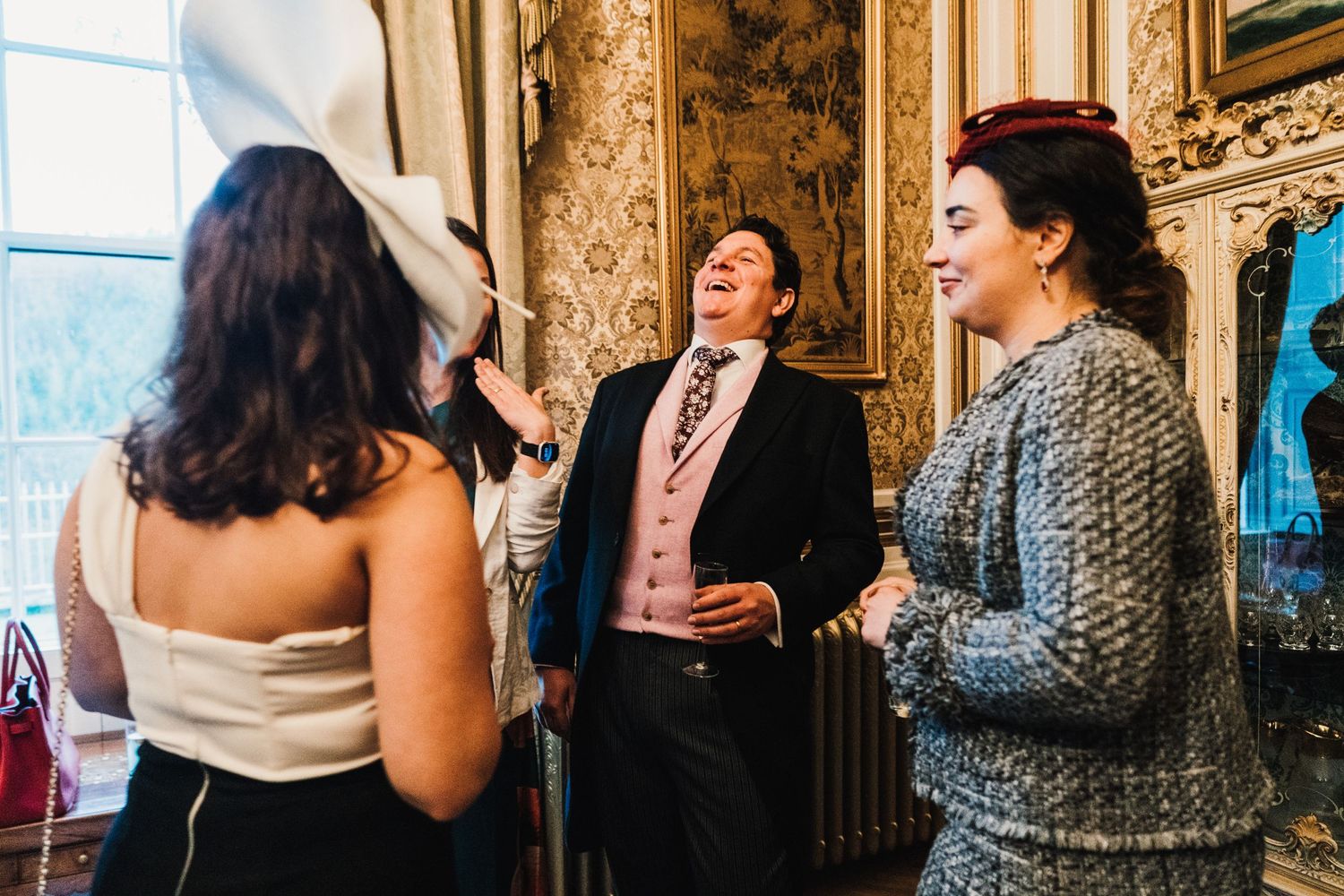 Wedding guests laughing and enjoying conversation in an elegant interior with ornate wallpaper.