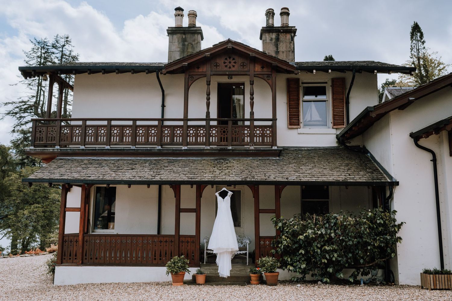 A white wedding dress hangs outside a rustic cottage with Tudor-style architecture.