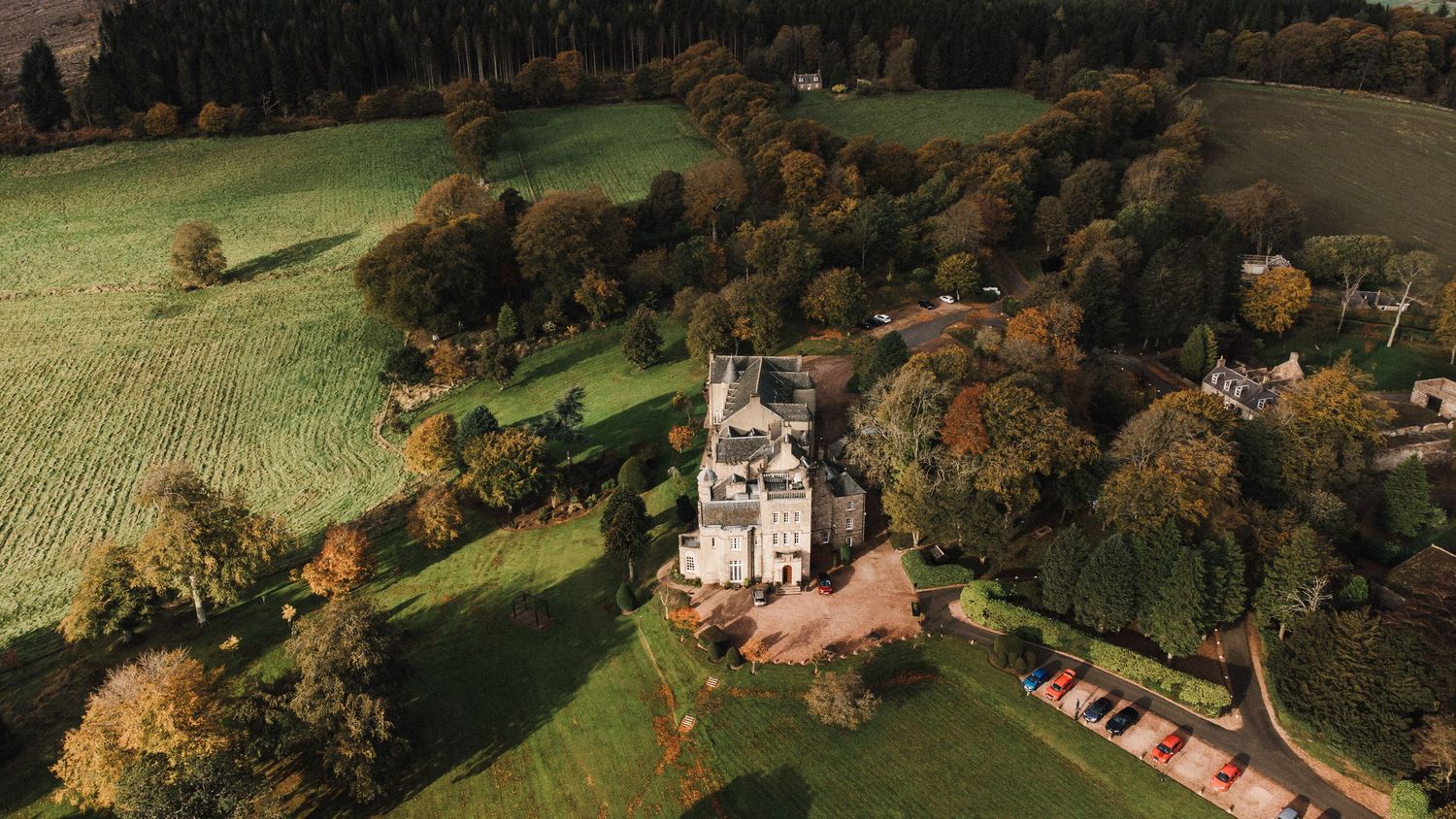 Aerial view of a grand castle surrounded by autumn trees and manicured lawns.