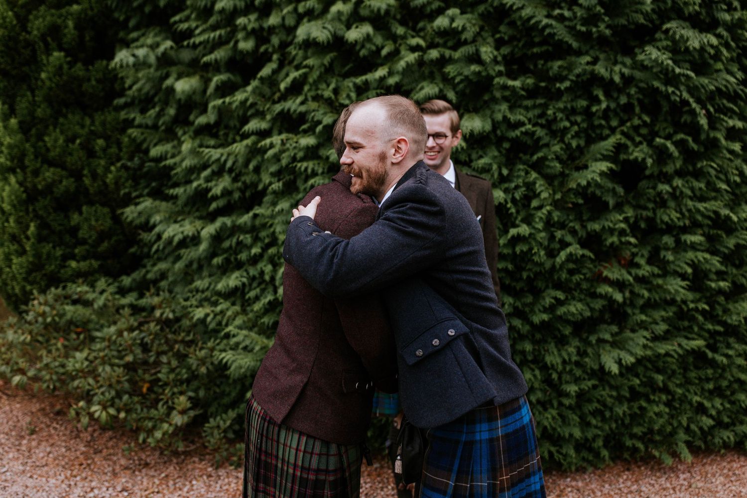 Wedding party members in formal attire share laughs on garden pathways.