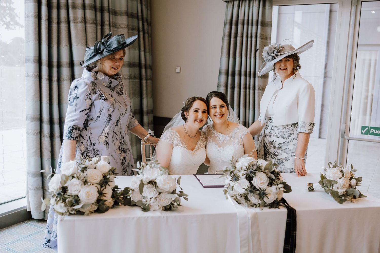 A wedding celebration with elegant floral arrangements on a white-clothed table surrounded by guests in formal attire.