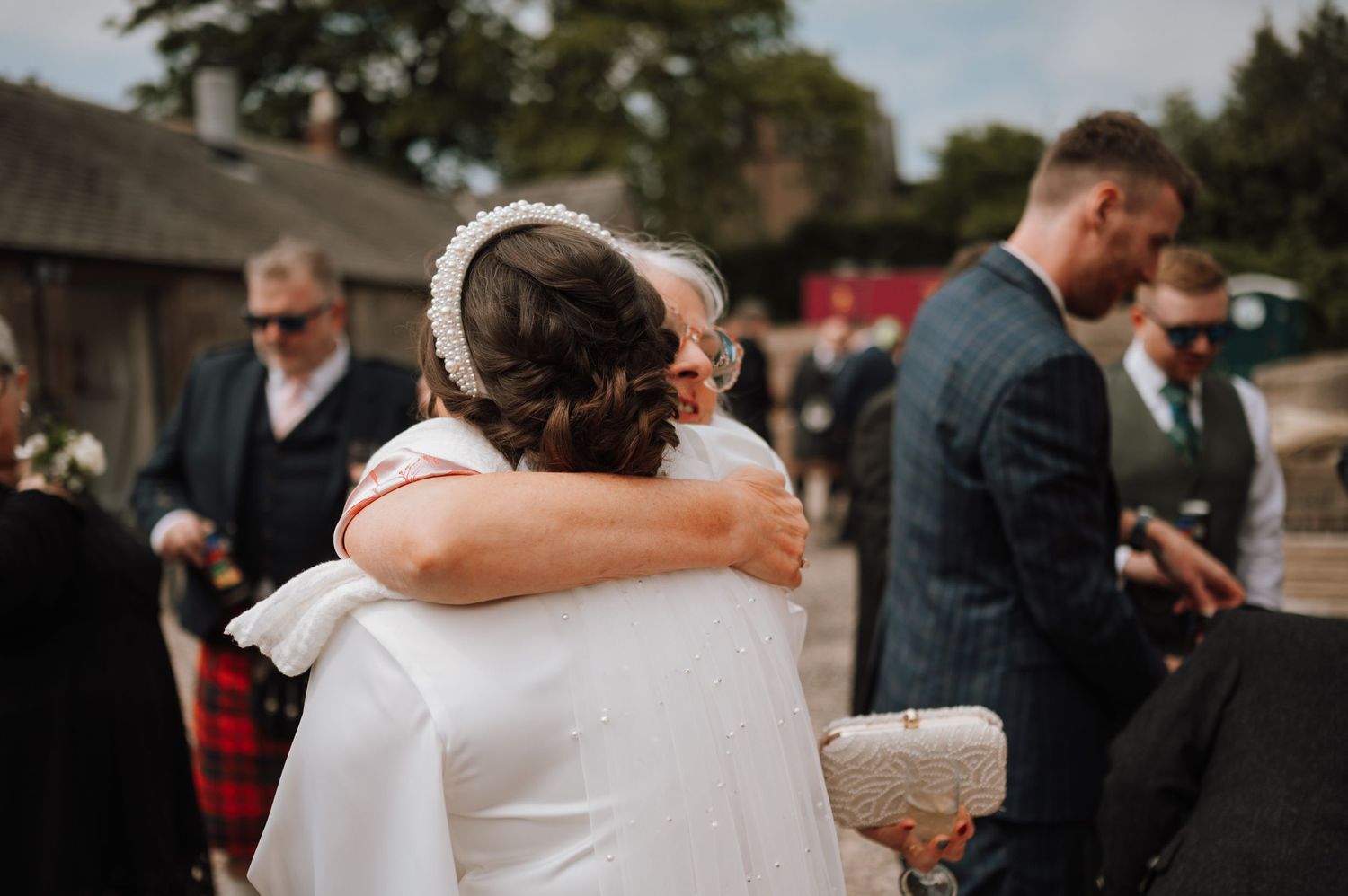 Emotional embrace during outdoor wedding reception near rustic buildings.