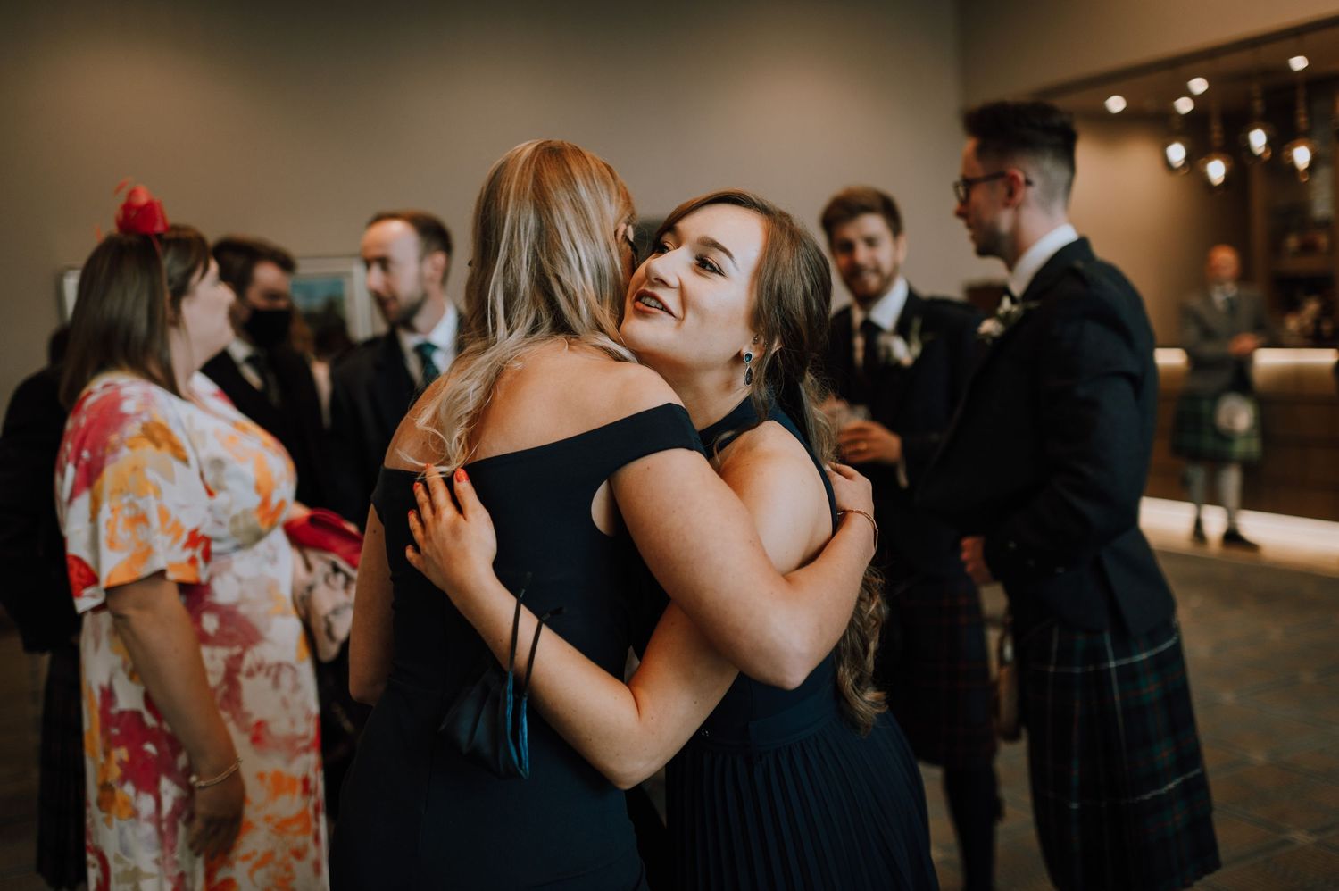 Wedding guests dancing and embracing at an indoor reception celebration.