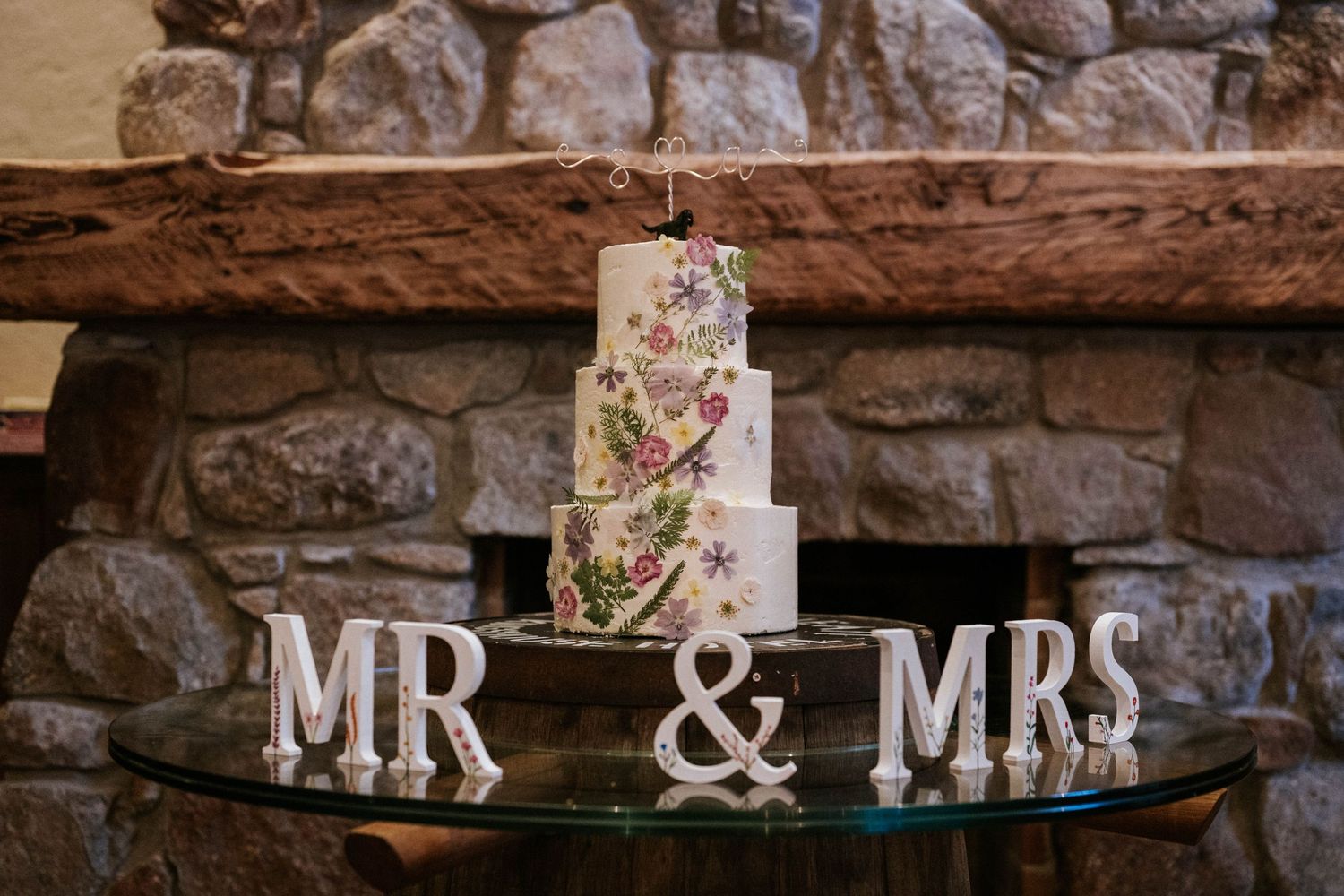 Rustic wedding reception decor with floral arrangements and Mr & Mrs sign on stone wall.