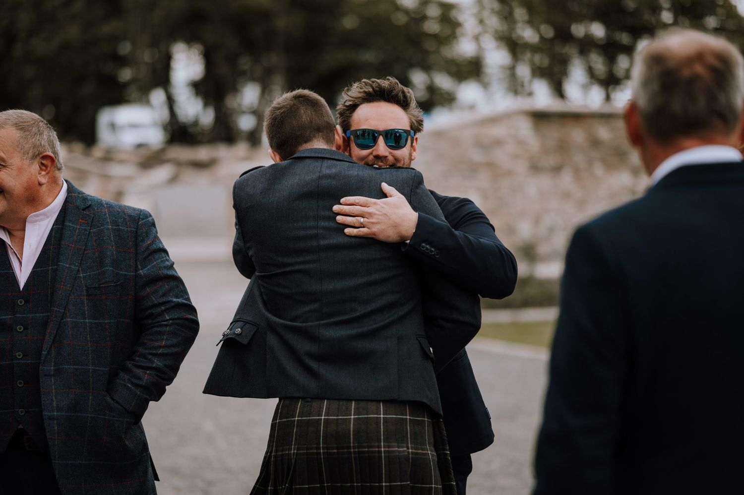 Heartfelt hugs exchanged between formally dressed guests at outdoor celebration.