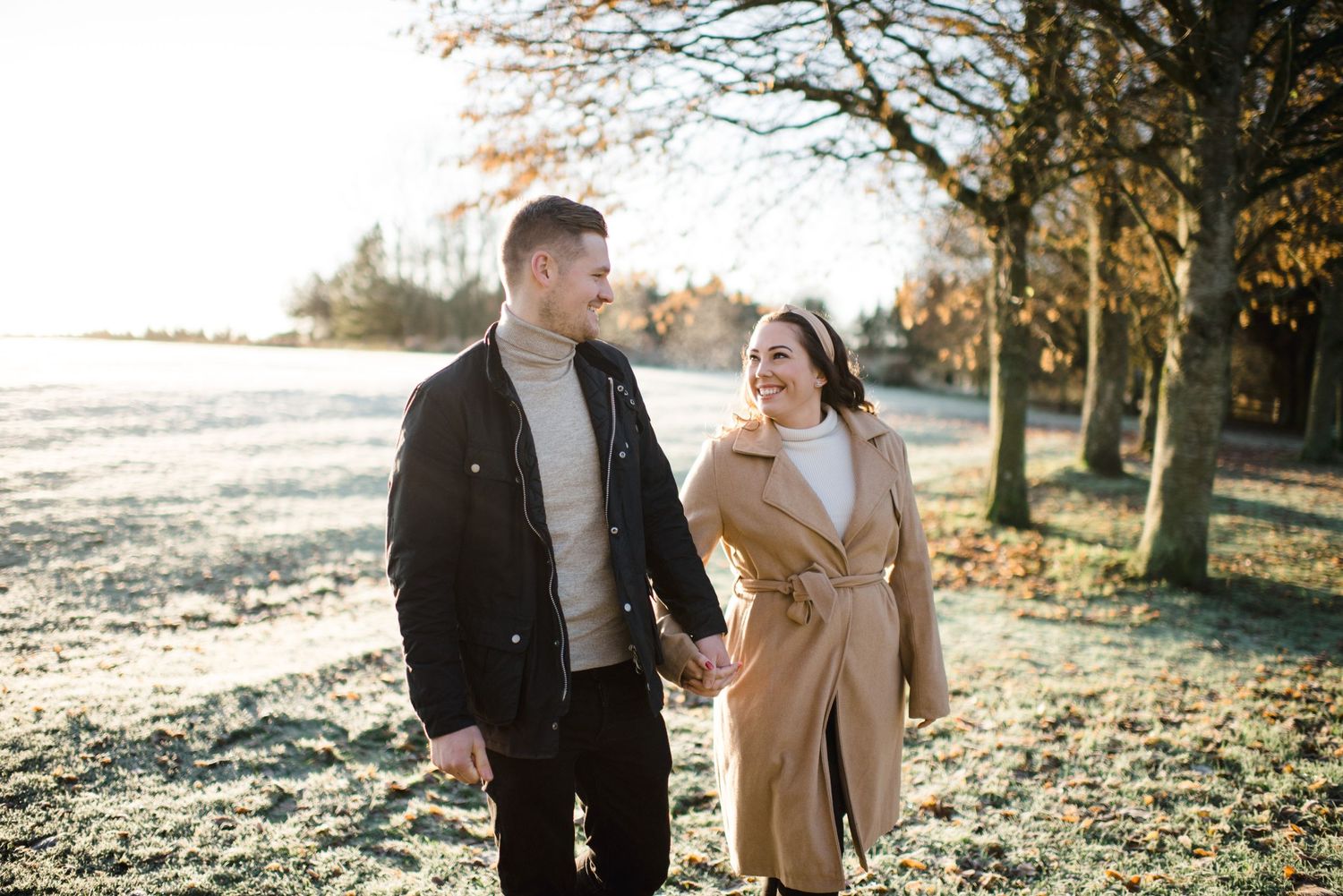 Couple walking through park on sunny autumn day wearing stylish coats.