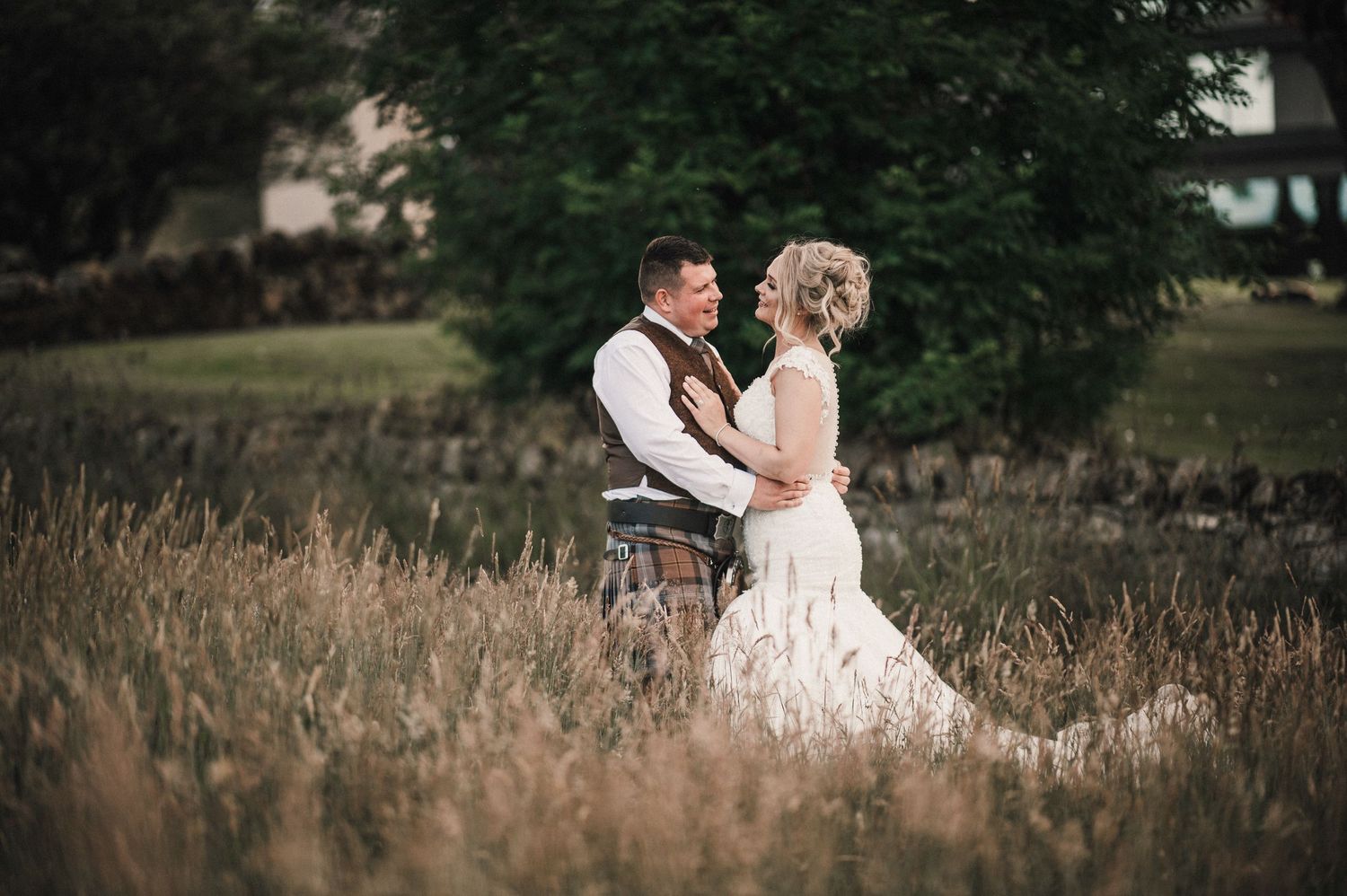 Romantic portrait of newlyweds standing in tall grass during golden hour.