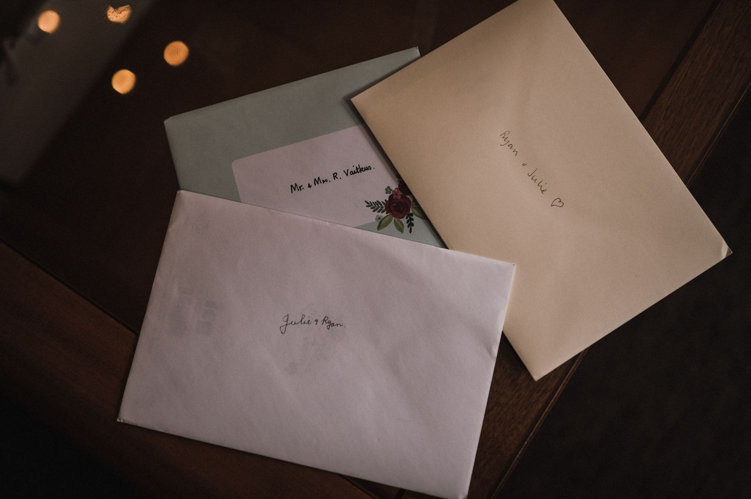 Three white envelopes with handwritten text arranged on a dark wooden surface with soft lighting.