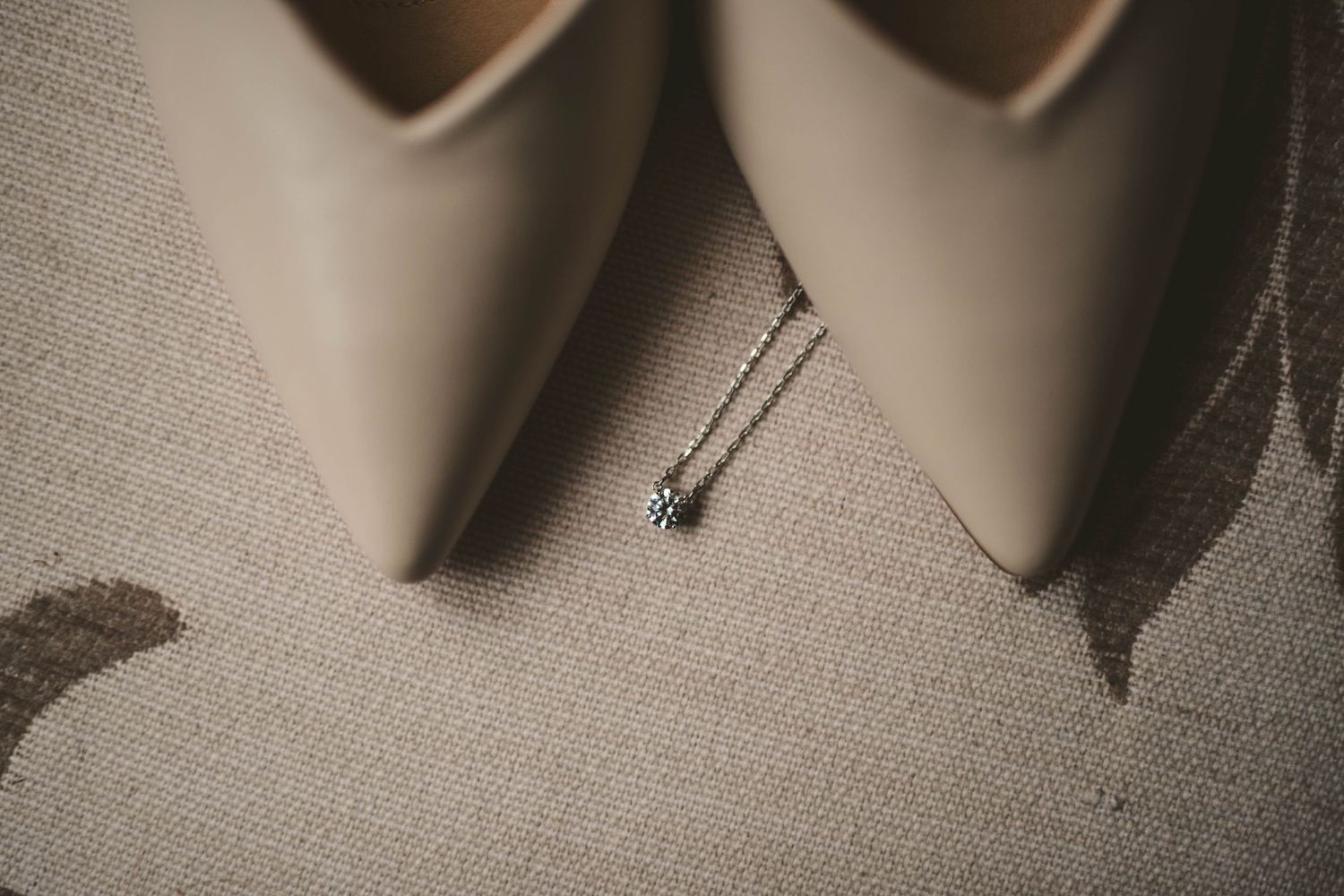 Close-up of pointed nude heels with delicate necklace placed between them.