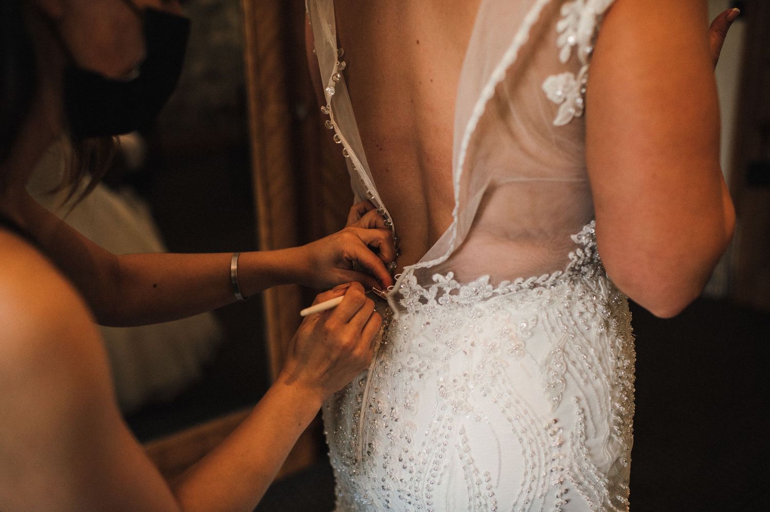 Close-up shot of wedding dress details being fastened, showing intricate beadwork and delicate lace.