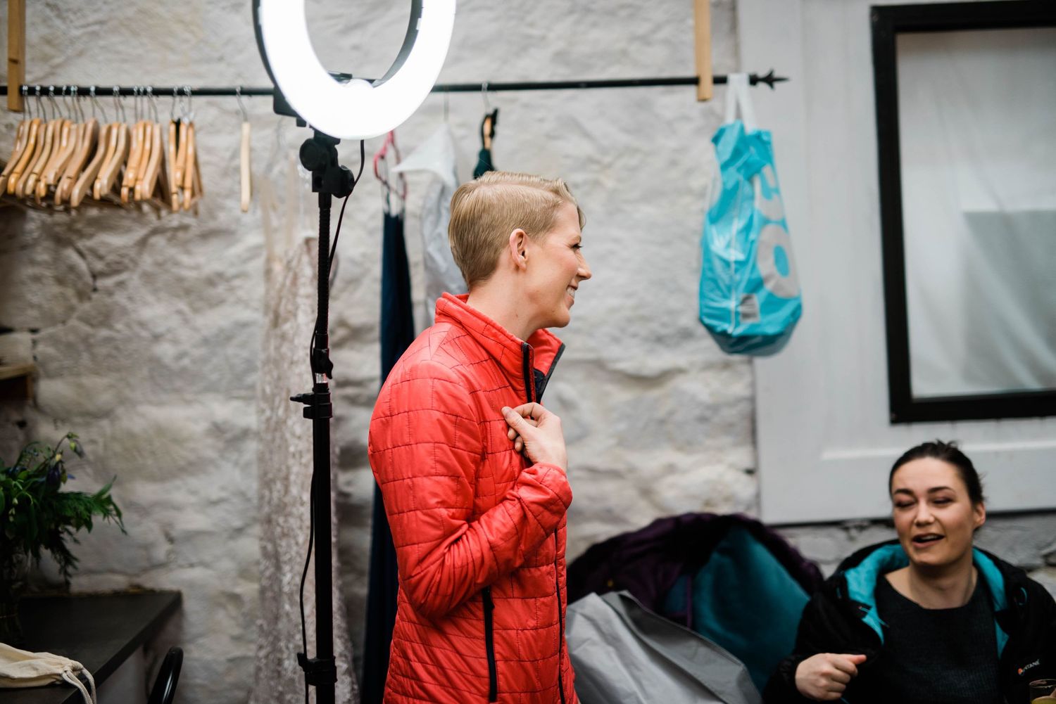 Interior preparation scene with lighting equipment and clothing racks against stone wall.
