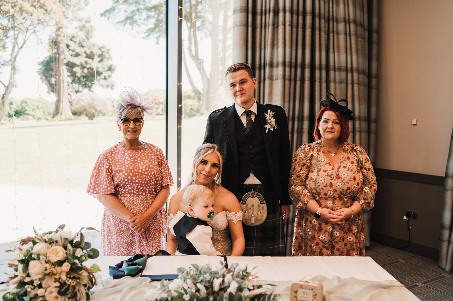 A formal wedding signing ceremony with guests in floral dresses and Scottish traditional elements.