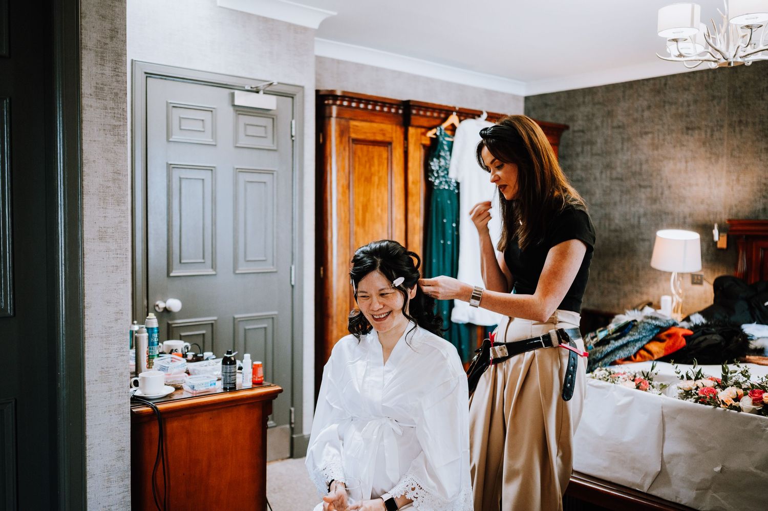 Wedding preparation scene showing hair styling in a cozy room with warm lighting.