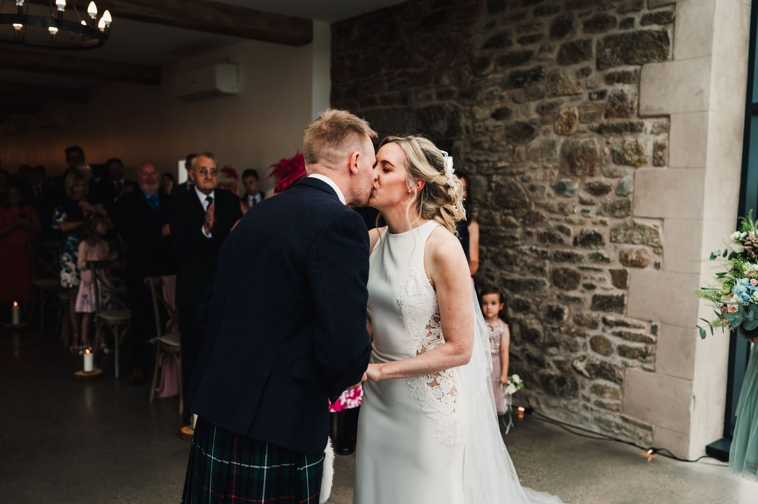 Romantic wedding moment in front of rustic stone wall under warm lighting.