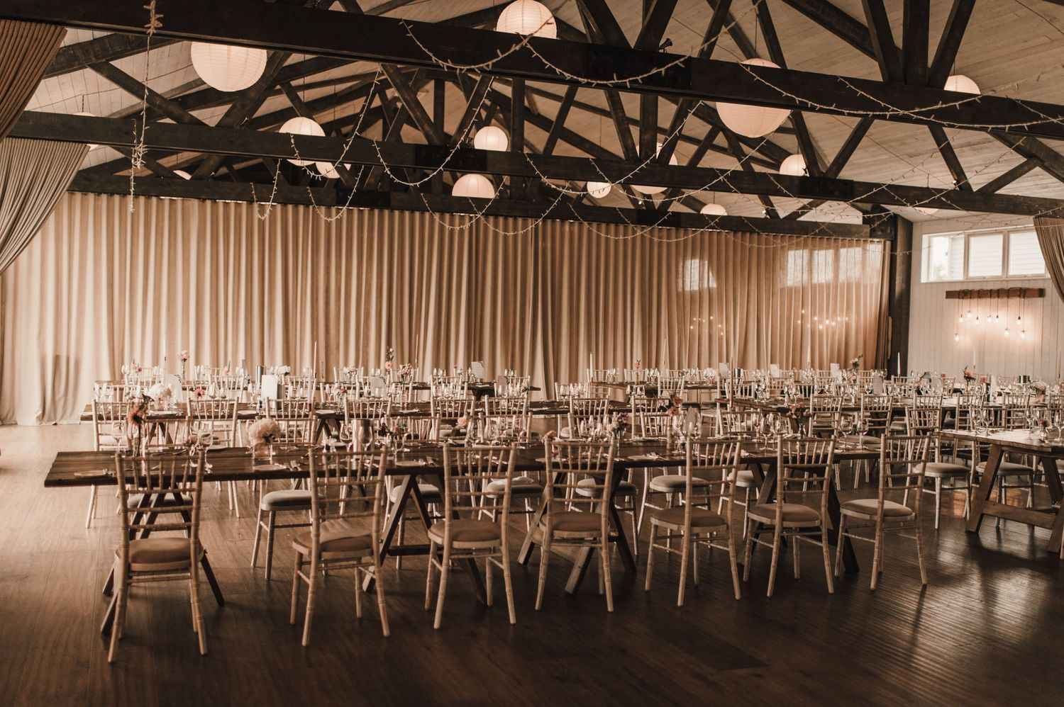 Large indoor event space with rows of chairs and exposed wooden ceiling beams in warm lighting.