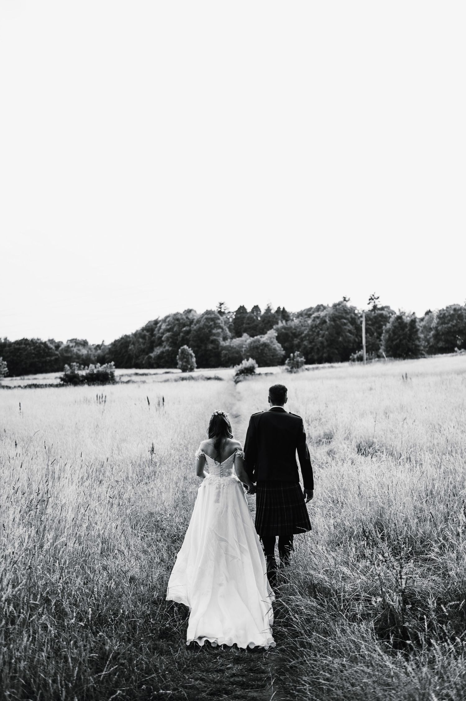 A black and white photo of newlyweds walking through a meadow.