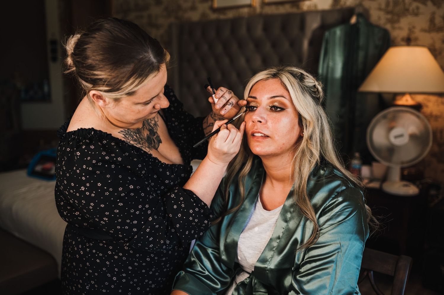 Professional makeup artist applying cosmetics in warm, intimate setting.