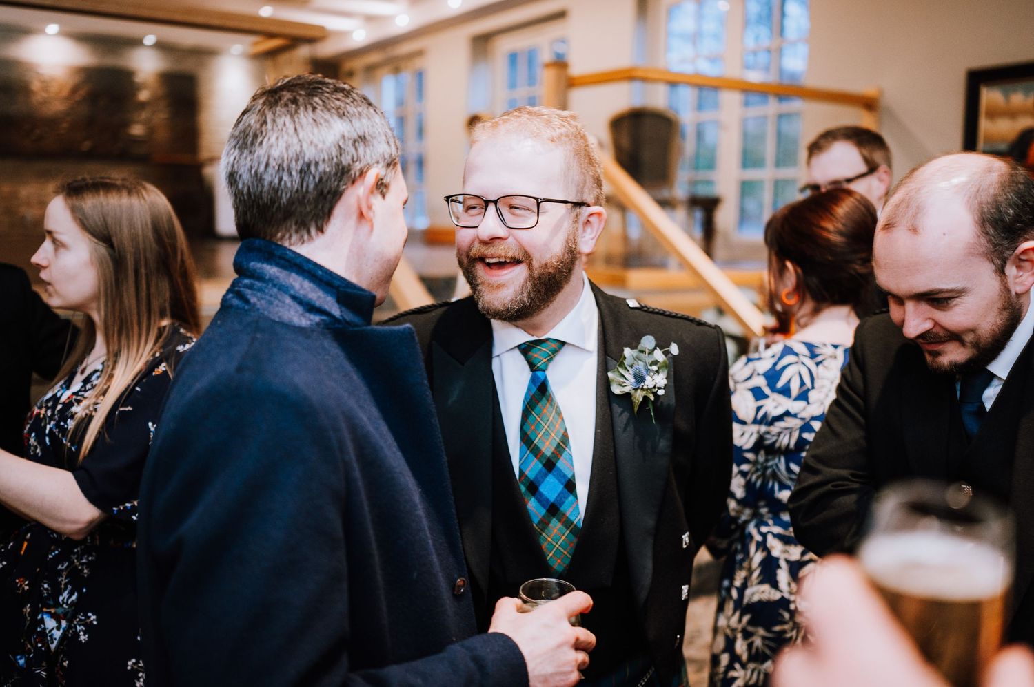 Guests wearing formal attire engage in animated conversation at an indoor reception.