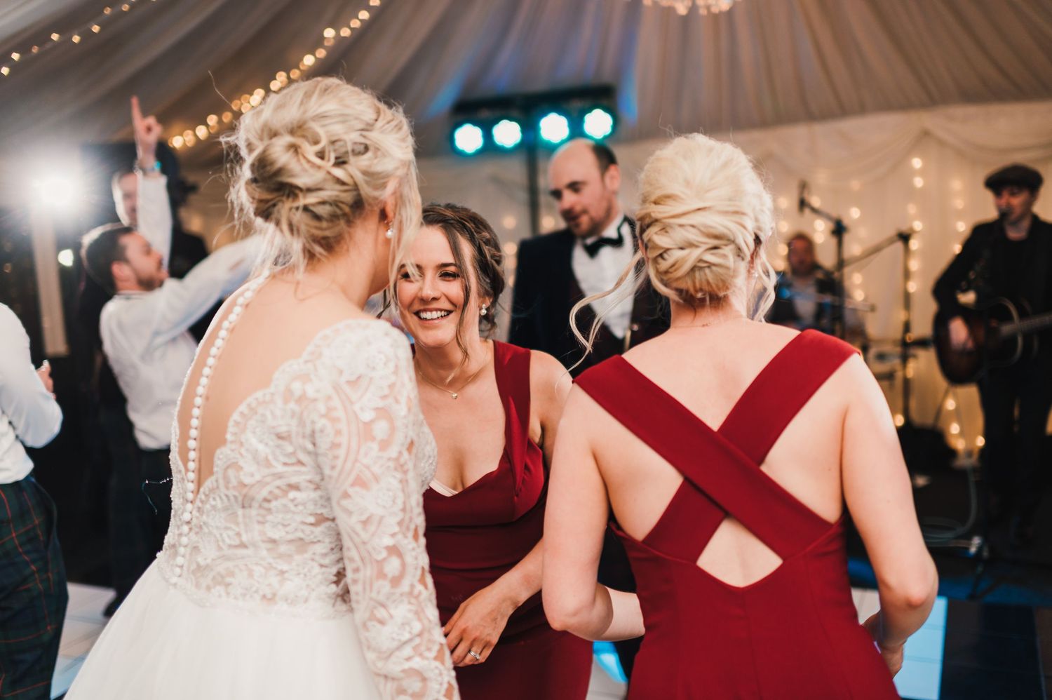 Wedding celebration features guests in formal attire dancing and laughing together under decorative lighting.