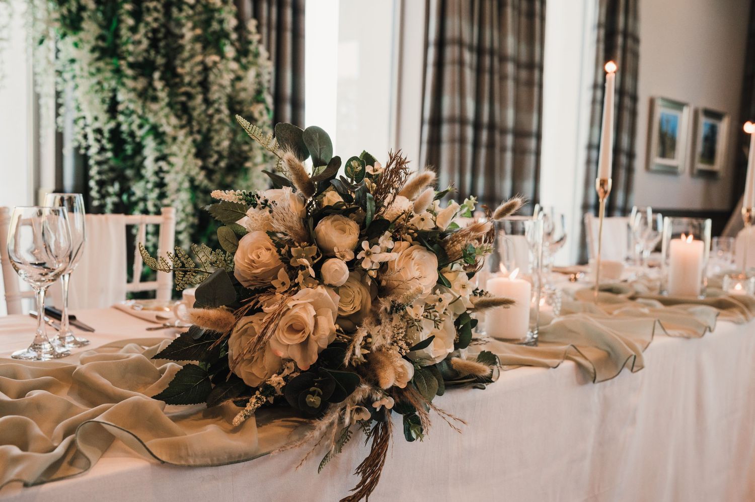 Romantic floral centerpiece with peach roses and greenery on white tablecloth.