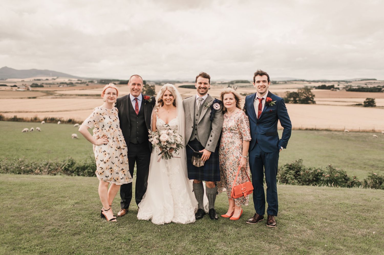 Wedding party stands together for formal portrait with scenic rural landscape in background.