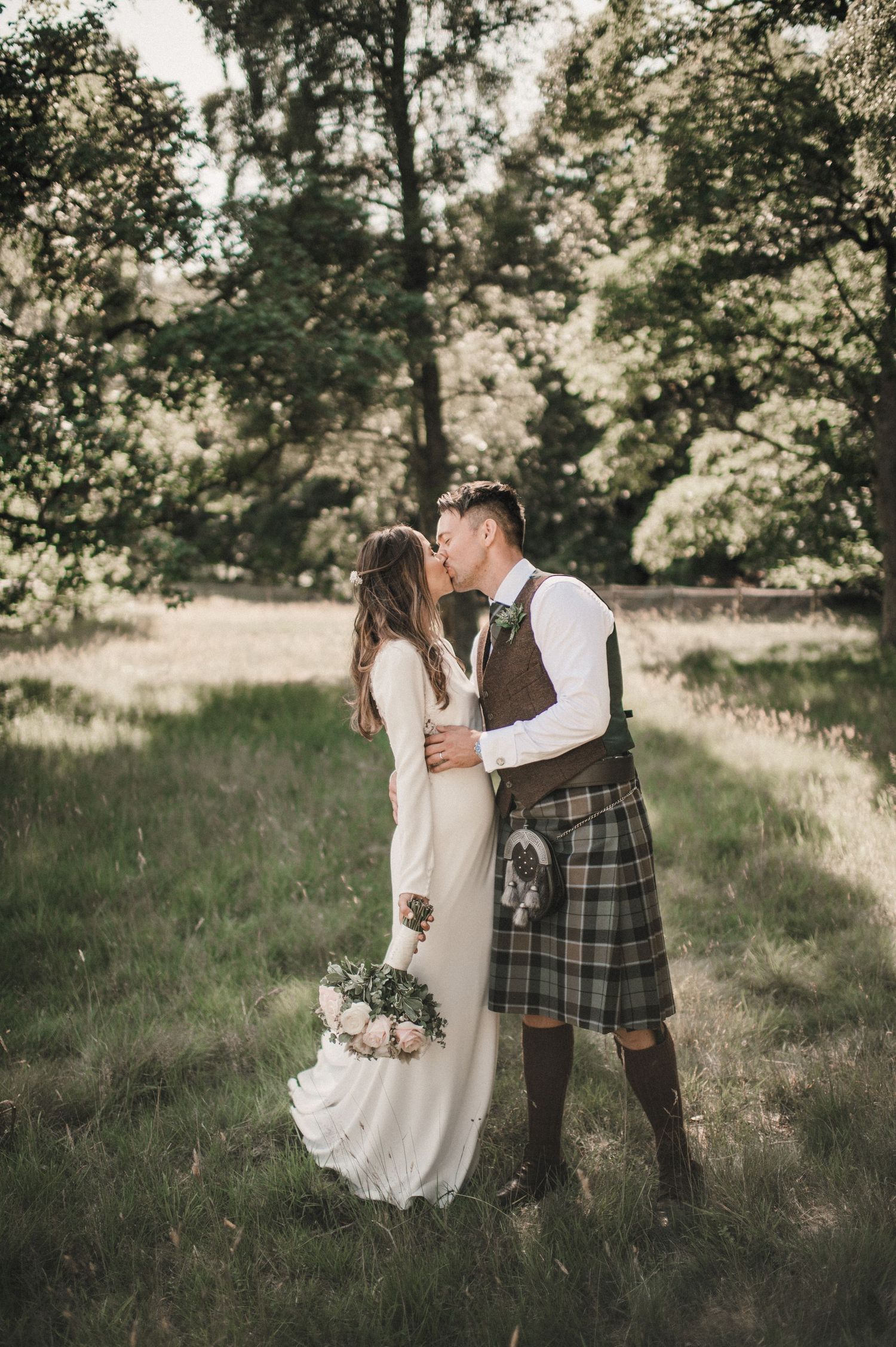 A romantic wedding portrait in a wooded setting with the couple embracing among tall trees.