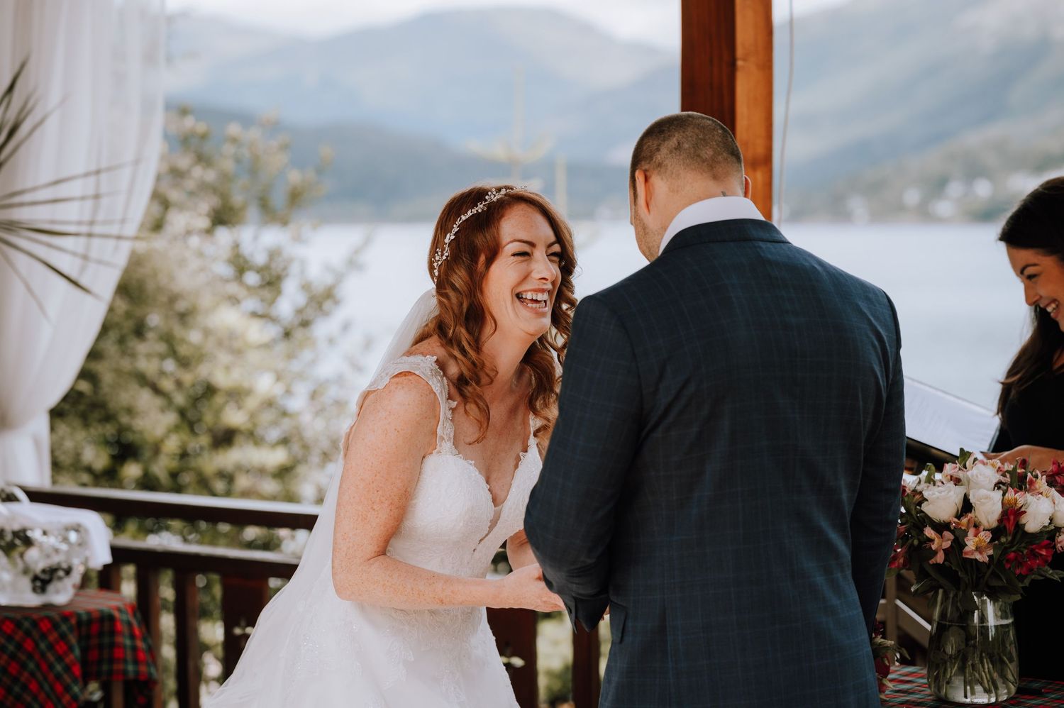 Bride laughs joyfully during outdoor wedding ceremony with groom and officiant.
