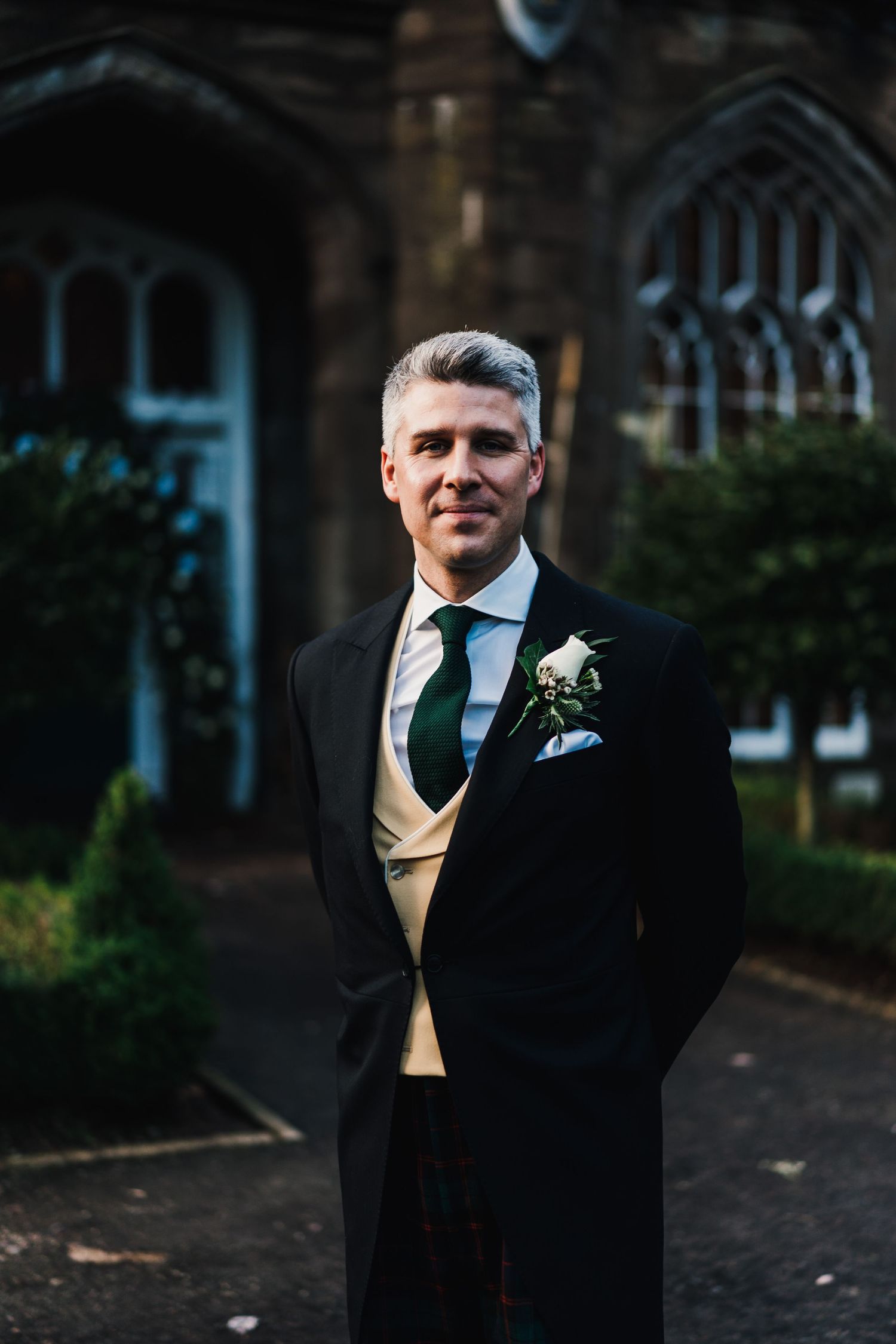 Formal portrait in front of gothic church architecture with boutonniere detail.
