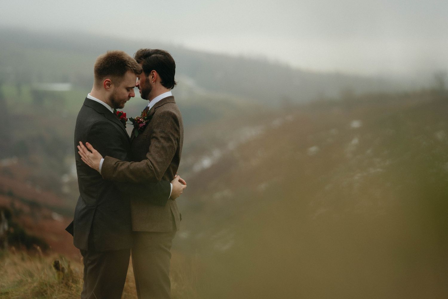 Two people embrace in an intimate moment against a misty mountainous landscape at dusk.