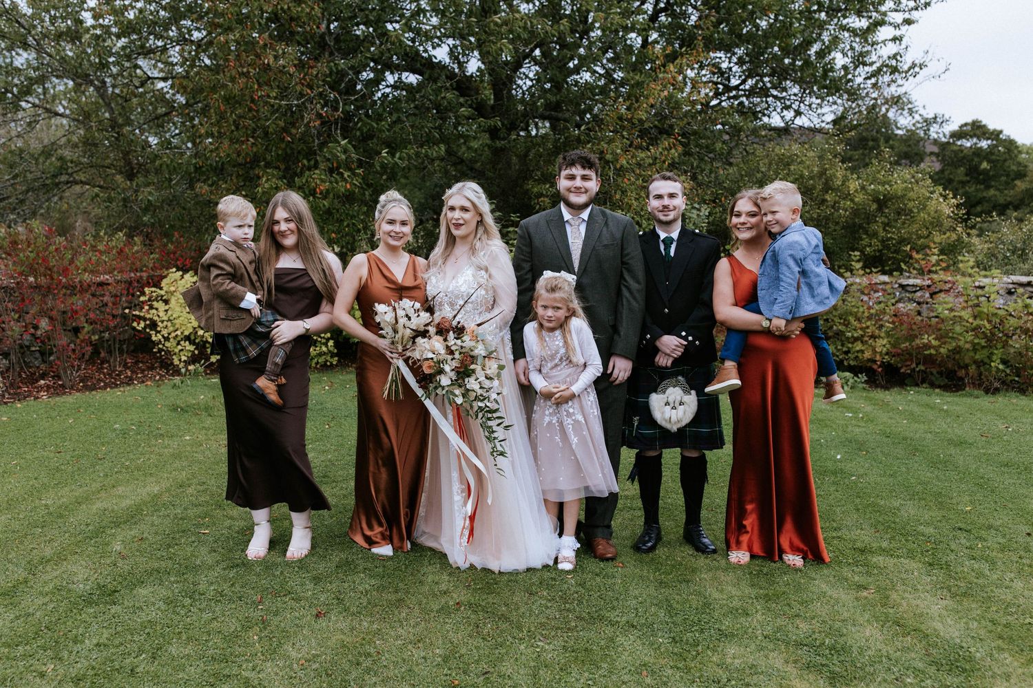 Wedding party posing for formal group photo on manicured lawn.