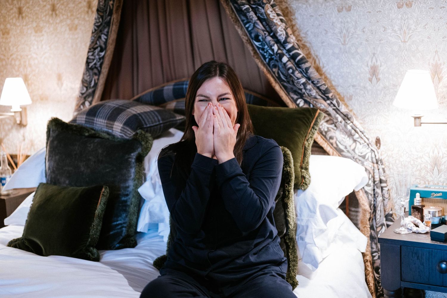 Person sitting on an ornate bed with decorative canopy and pillows.