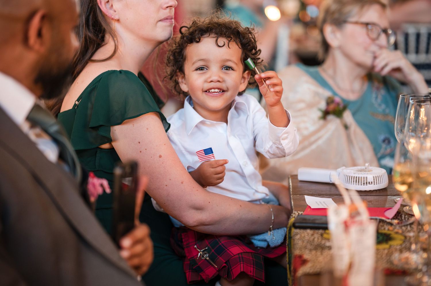 Wedding reception guests share joyful moments at dining tables during evening celebration.