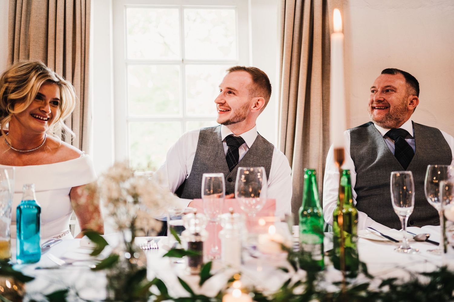 Wedding reception dining tables set with glassware and decorations in a bright indoor space.
