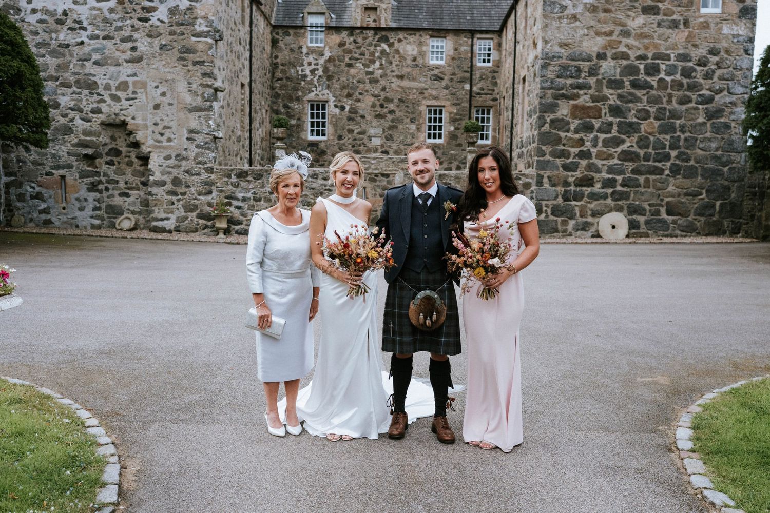 Wedding party gathered outside a historic stone building.