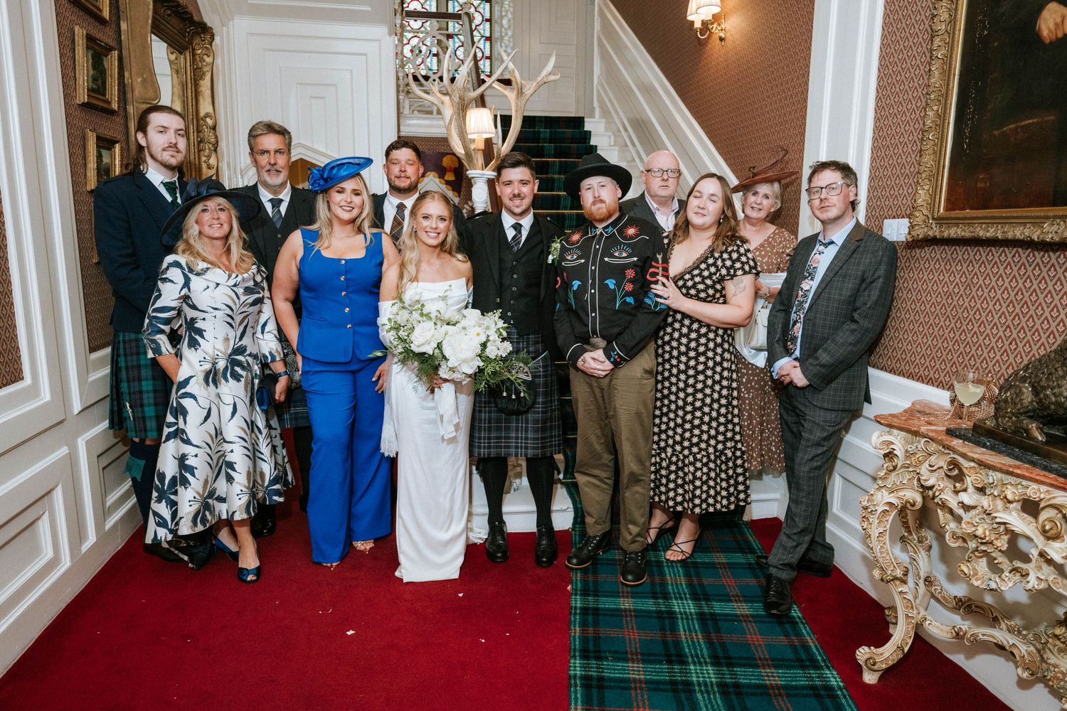 Wedding guests pose for formal group photos in an ornate indoor venue.