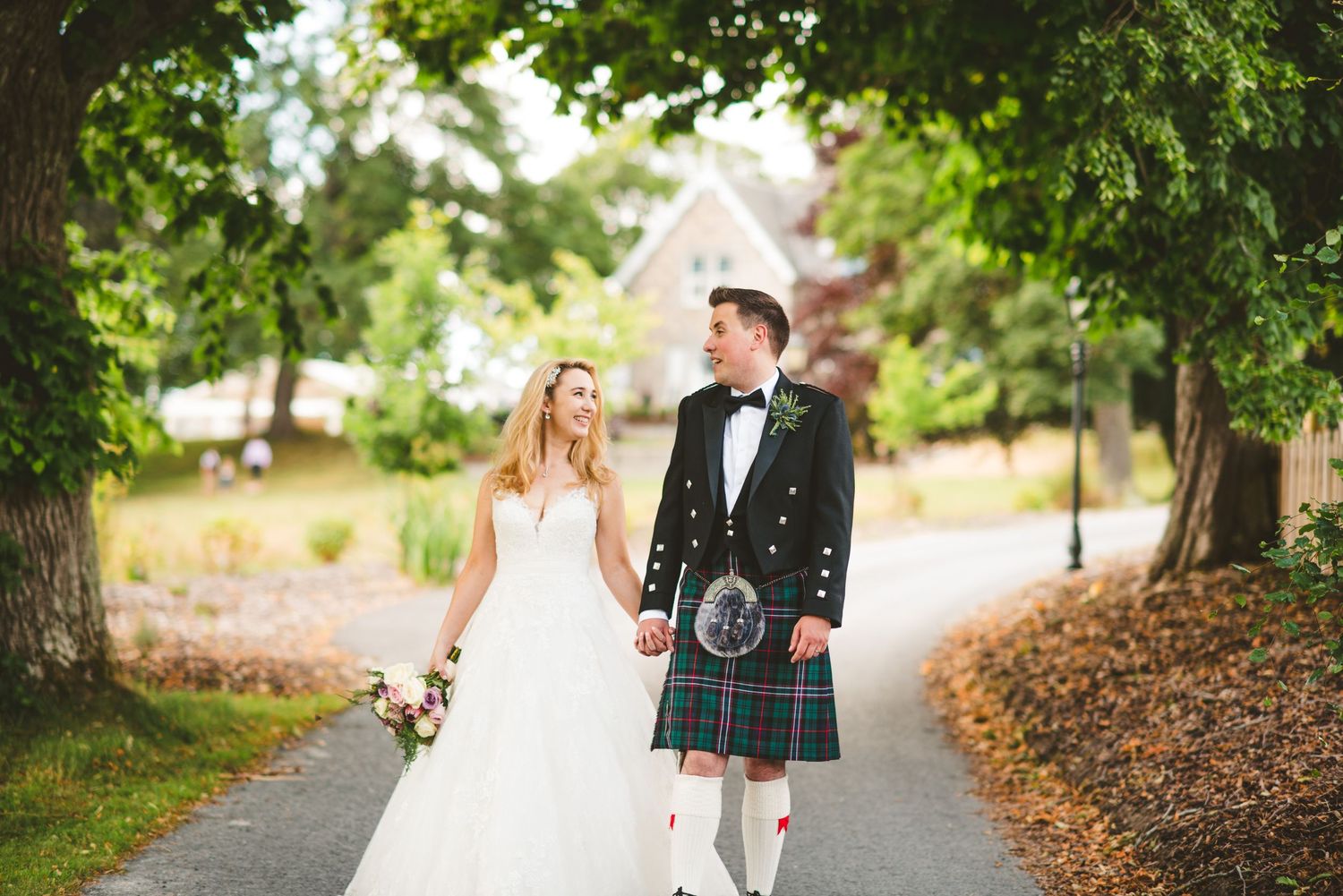 Wedding couple walking hand in hand down a tree-lined autumn path.