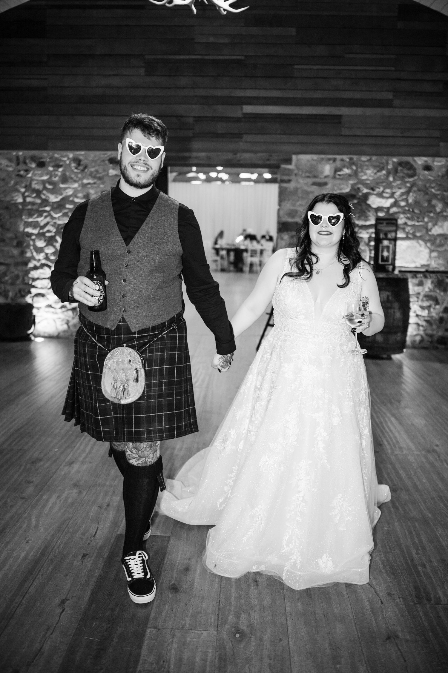 A black and white wedding photo series showing a couple in sunglasses walking on a wooden dance floor.