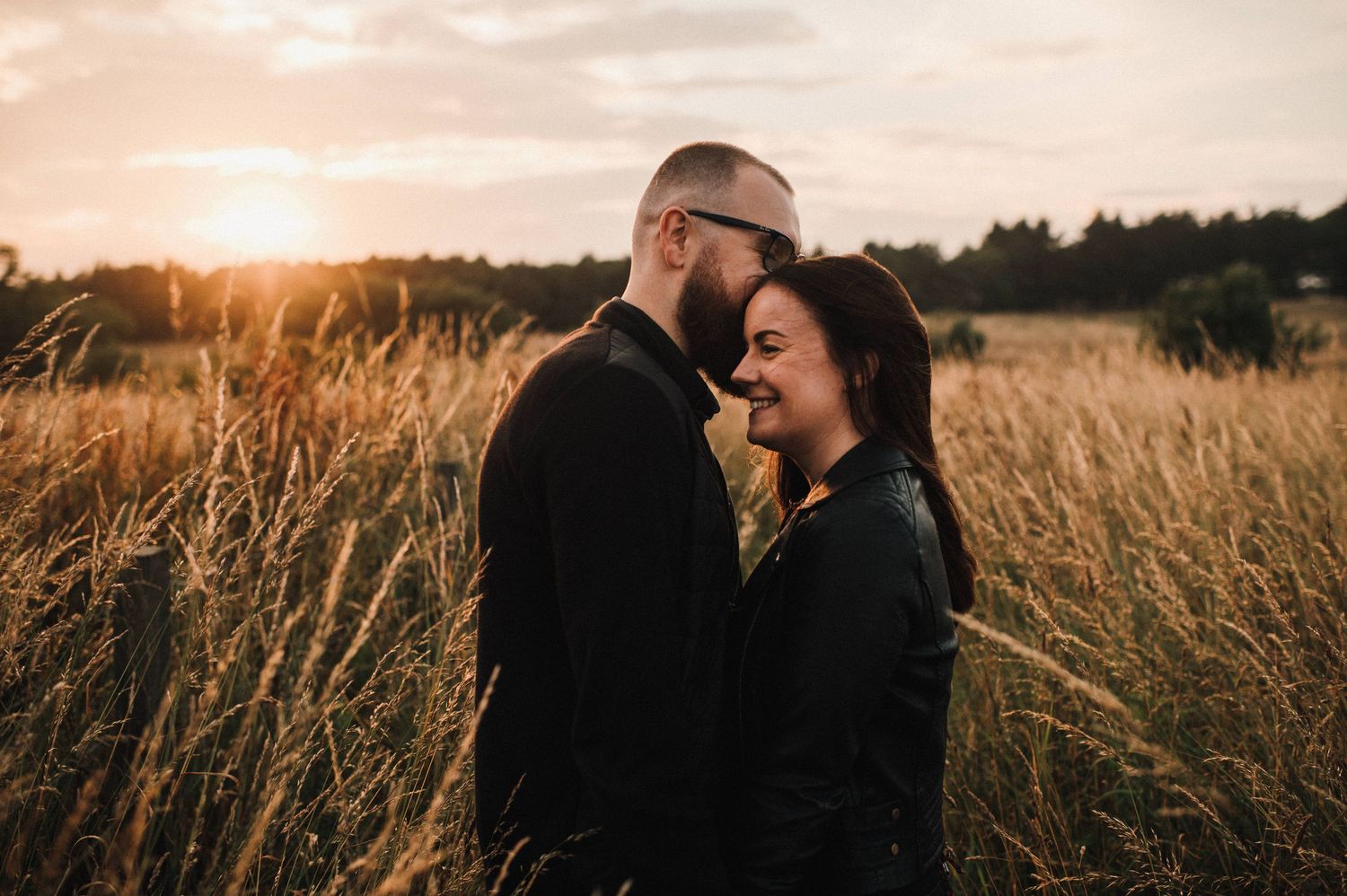 Intimate couple shares tender moment in wheat field at sunset during engagement photo session.