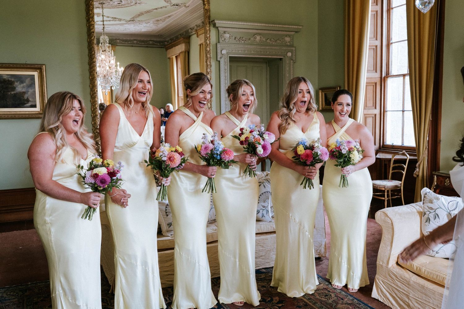 Row of bridesmaids in cream-colored dresses standing together in an elegant room.