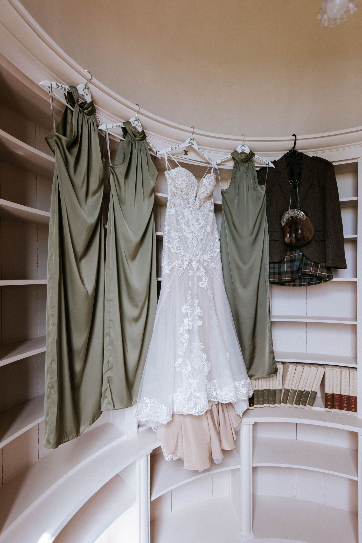 Wedding dress displayed among sage green bridesmaid dresses in curved alcove.