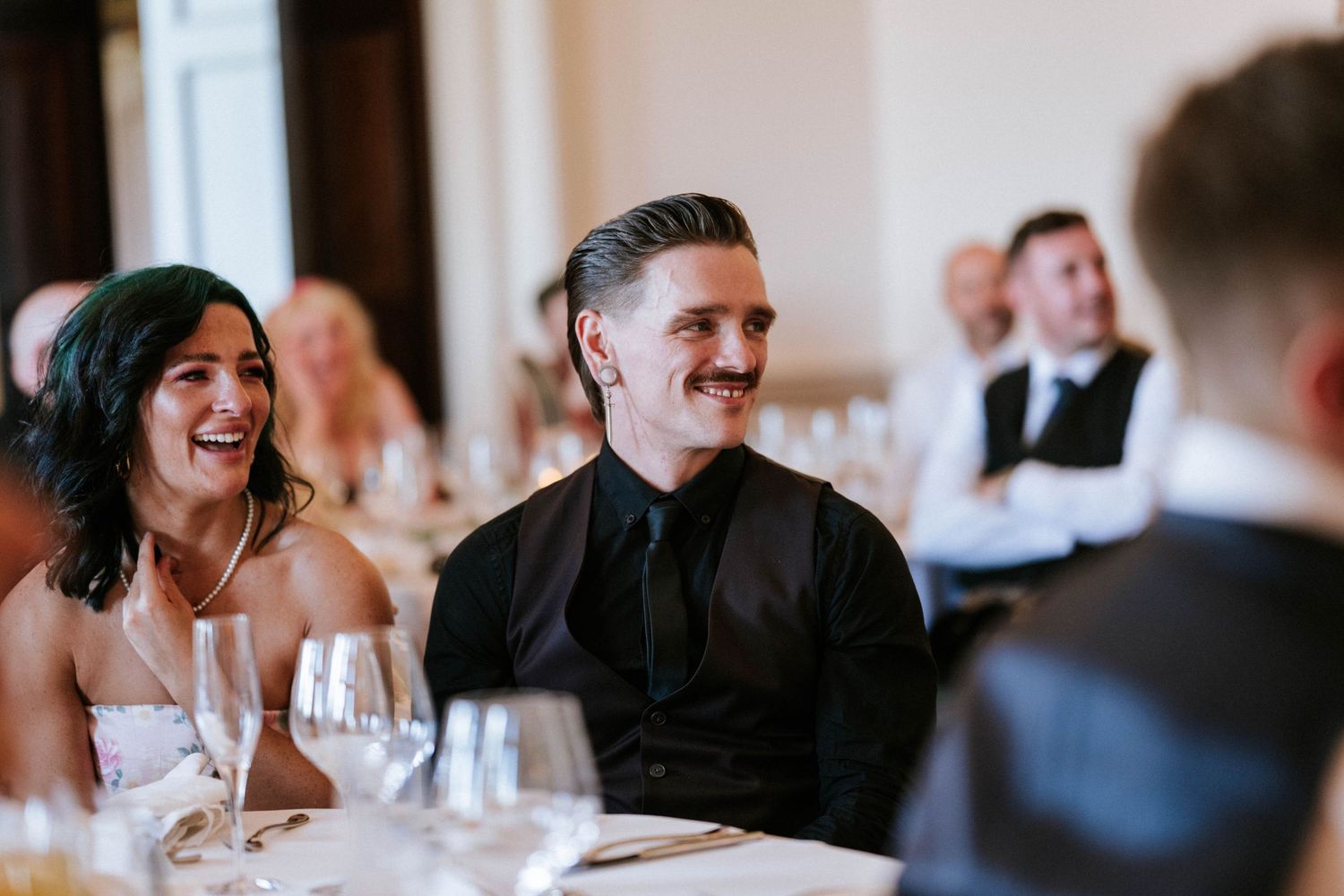 Candid moment of laughter shared between guests at wedding reception dinner table.