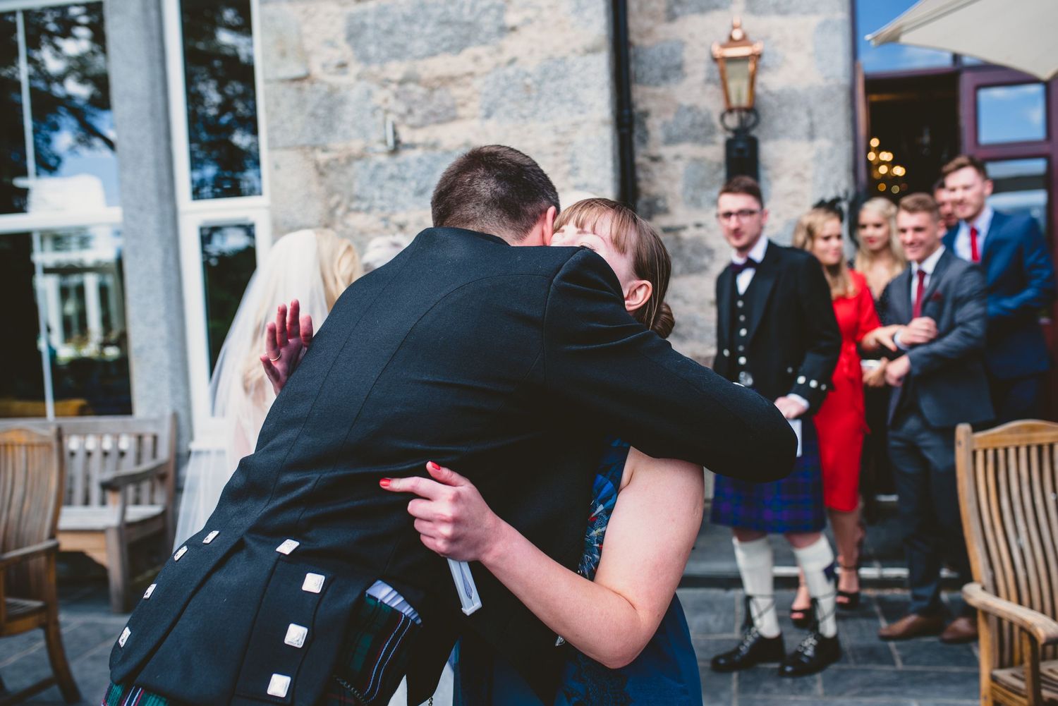 Wedding party celebrating outside stone building in traditional Scottish formal wear.