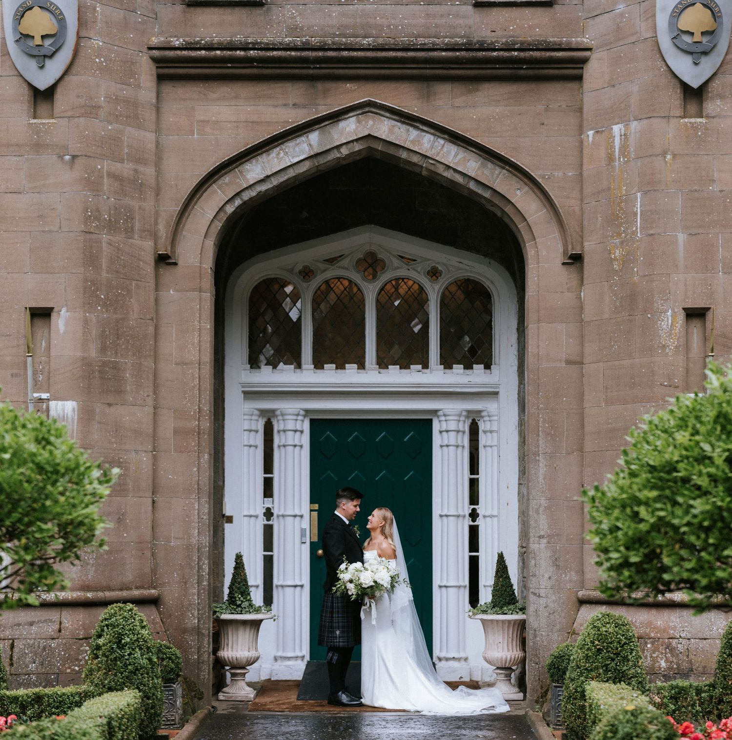 Elegant wedding couple poses in front of historic stone church entrance with Gothic archways and white columns.
