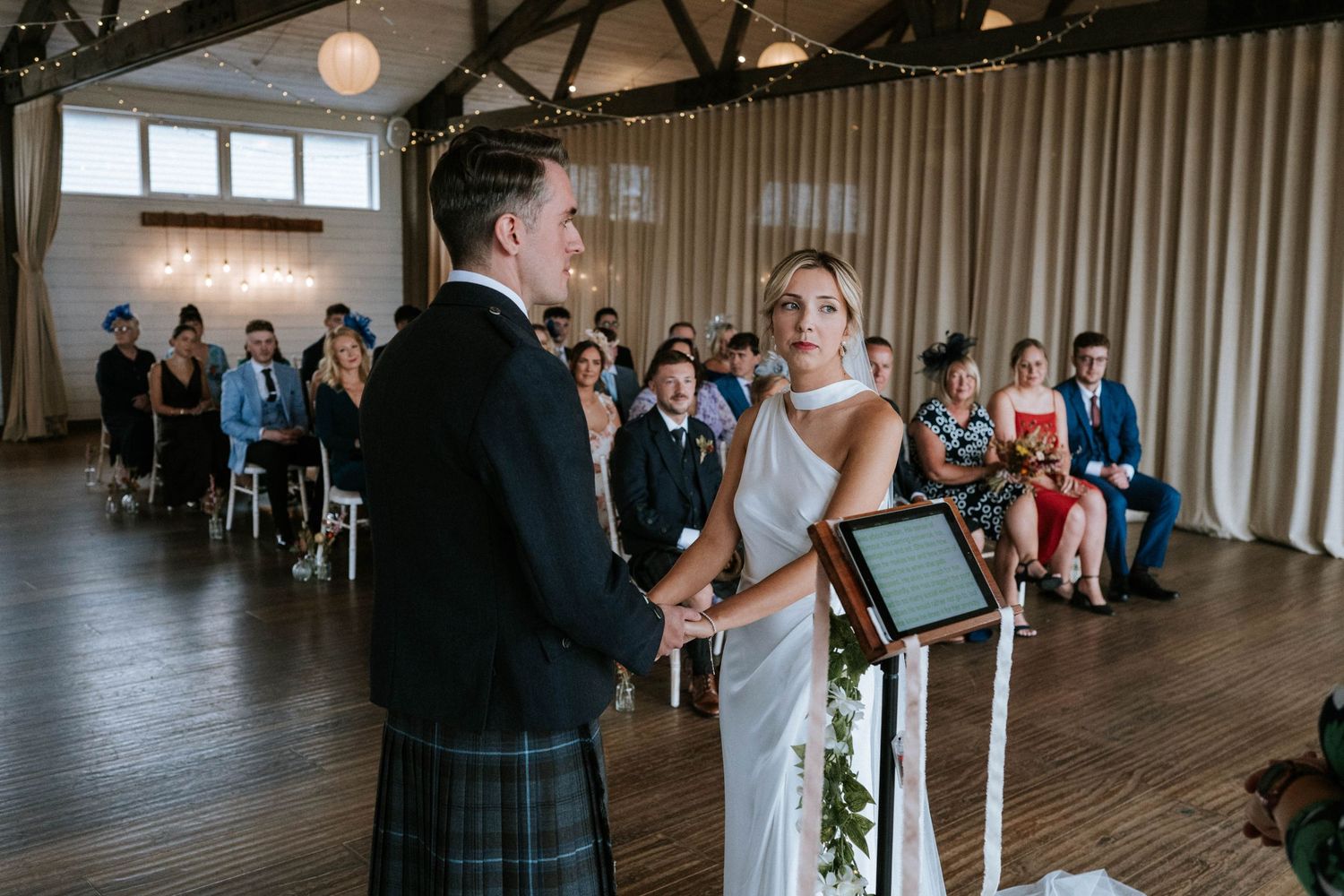 Wedding guests mingle and socialize during an indoor reception in an elegant venue with wood beam ceilings.